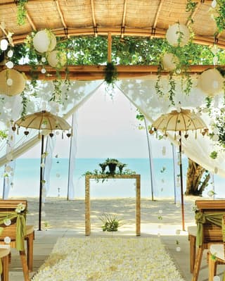 Bamboo pergola over a beach set with rows of chairs and an aisle for a wedding