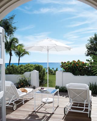 An arched doorway opens onto a private decking, furnished with sun loungers and surrounded by lush gardens and sea views