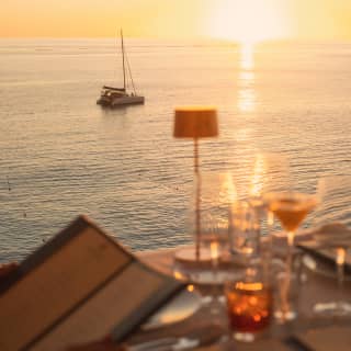 In soft-focus, an off-camera guest peruses the L'Oursin menu at an outside table, as the sun sets on the ocean horizon.