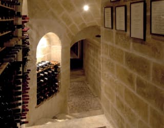 View through a softly-lit stone corridor with an arched ceiling and alcoves of wine racks, with steps down to the cellars.
