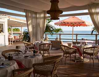 View of the deck at Laplaj where round tables with wicker chairs enjoy canopy shade and extraordinary ocean views.