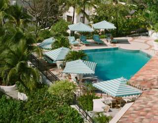 Looking down on the turquoise pool, half-obscured by rooftops, lined with six blue and white-striped parasols and loungers.