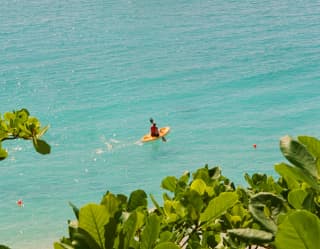 High angle view of the sapphire waters where a kayaker paddles parallel to the bay in front of two anchored sailing boats.