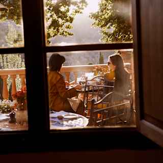 View from inside Miró restaurant to the terrace where two women sit in golden light at a table, enjoying incredible views.