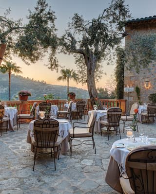 Stone-tiled restaurant patio dotted with formal candlelit tables at sunset