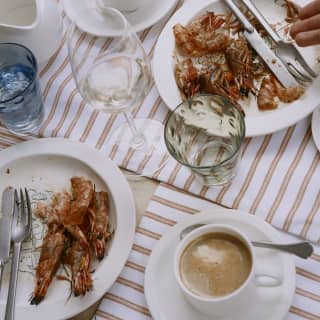 Looking down on a satisfied dining table, where fresh coffees sit by finished plates of prawns and glasses of water and wine.
