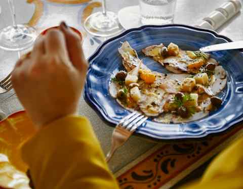 A guest rests her hands on the table by her lunch of focaccia, grilled vegetables and olives, served on a blue china plate.