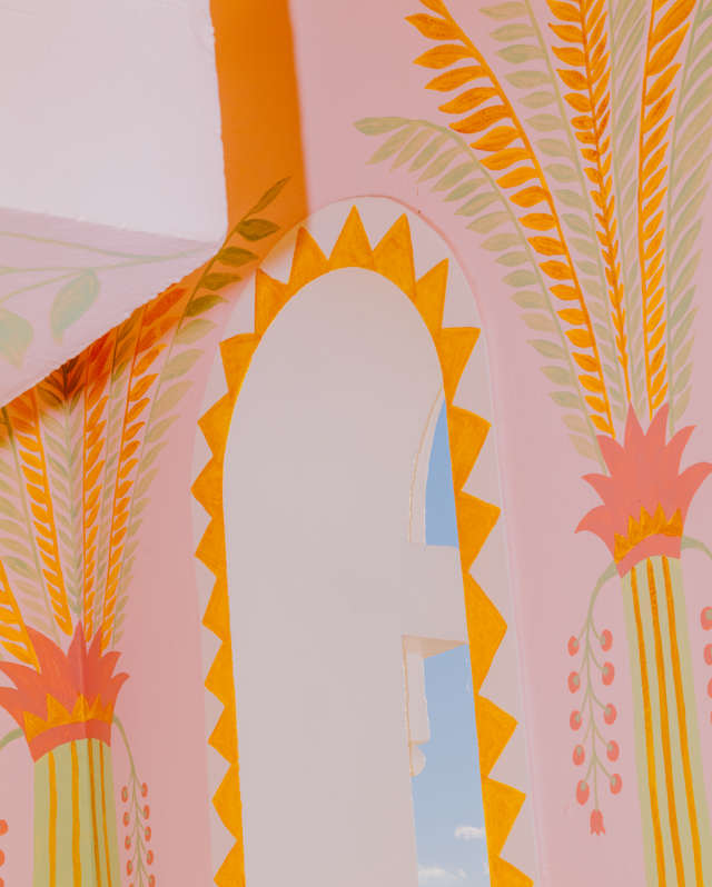 Close-up of a wall arch with a border of hand-painted triangle patterns and palms, done in pinks, oranges, and greens.