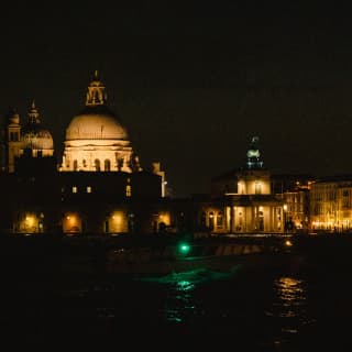 The Basilica Santa Maria and the Doge's palace create a parade of grand, warm-lit edifices, seen from the canal at night.