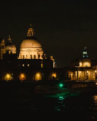The Basilica Santa Maria and the Doge's palace create a parade of grand, warm-lit edifices, seen from the canal at night.
