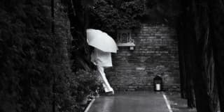 A guest dressed in white, carrying a white umbrella, disappears down a passageway in the hotel grounds, in black and white.