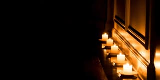On Earth Day, a row of five lit tealights on a shelf provides light in the darkness, illuminating the wood-panelling behind.