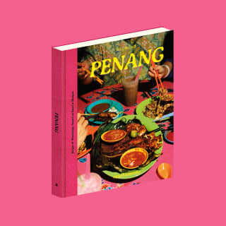 Belmond's Eat Your Way Through Penang cookbook, with a vibrant cover of dishes and diners, pictured on a pink background.