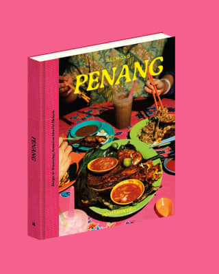 Belmond's Eat Your Way Through Penang cookbook, with a vibrant cover of dishes and diners, pictured on a pink background.