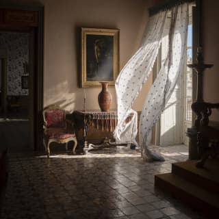 Breeze billows in diaphanous door drapes, bringing sunlight and movement into a darkened, cool room in Palazzo Castellucio.