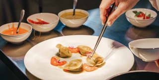 A fine dish of seafood pasta is assembled on a simple white plate on a shiny steel kitchen worktop
