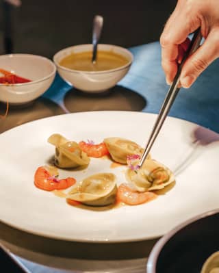 A fine dish of seafood pasta is assembled on a simple white plate on a shiny steel kitchen worktop