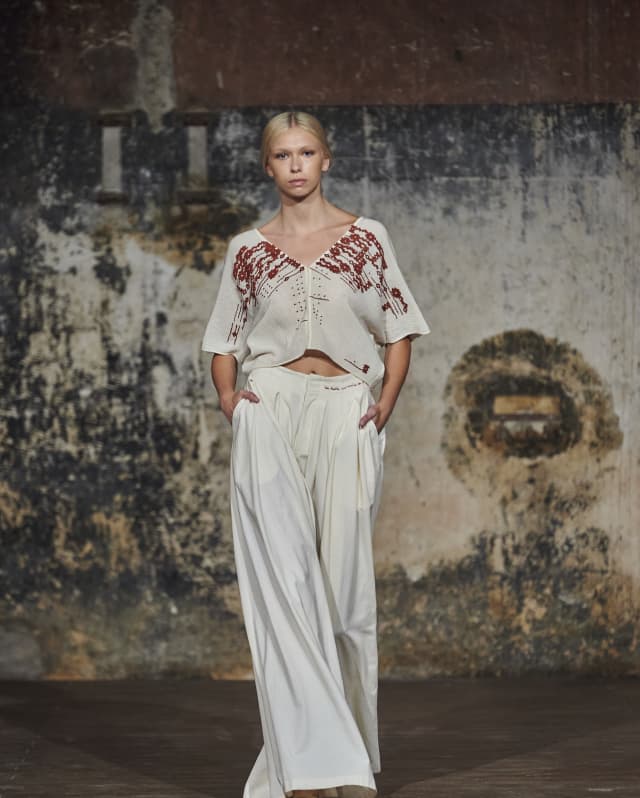 A model wears white, wide-legged Mercedes pants and cropped top with red embroidery and detailing, by Collectiva Concepción.