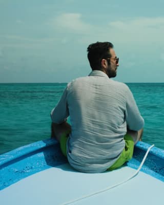 Maroma Executive chef, Daniel Camacho sits on the prow of a blue and white boat in Yucatán's sapphire sea, seen from behind.