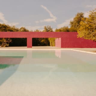 View over a shallow pool to a red wall with two flat arches belonging to the Cuadra San Cristóbal by architect Luis Barragán.