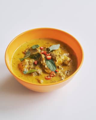 Close-up of Panang Curry with meat and slices of red chilli and curry leaves, served in a yellow bowl, seen from above.