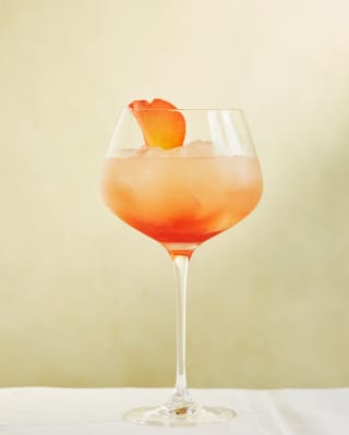 A rose petal garnishes a Portofino Spritz, which looks like sunset in a glass, with lemon juice, gin, rose liqueur and syrup.