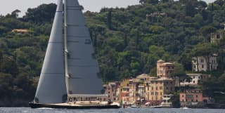 A yacht sails past pastel painted waterfront villas and lush green woods of Portofino