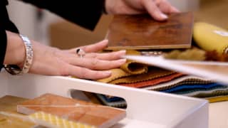 A hand, belonging to Rachel Johnson, senior studio director at Wimberly Interiors, rests on fabric swatches and wood samples.
