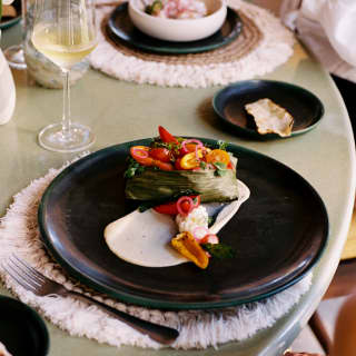 Tamale - a corn dough steamed in a husk - is served at Casa Mayor on a black plate, garnished with fresh tomato and capsicum.