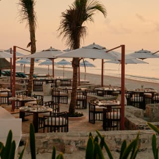 Side view of dining tables and cantilever parasols on Casa Mayor's terrace, ready for guests in the peach light of sunset.