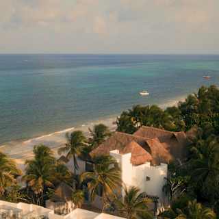 Sweeping aerial view of Maundays bay, where two boats bob on azure waters which roll onto Maroma's palm-fringed beach.