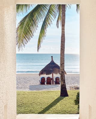 Thatched parasol over three sunbeds overlooking white sands and a calm sea