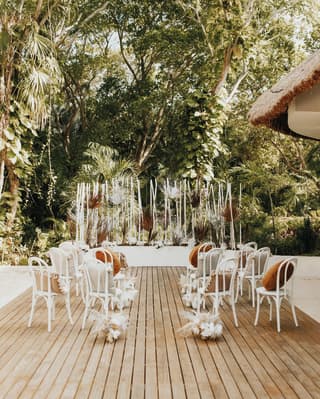 On a wooden deck surrounded by jungle, a registry table and witness chairs with white flourishes await a memorable ceremony.