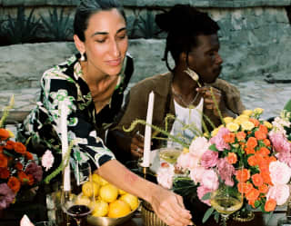 A guest reaches across the table with floral decorations to taste her friend's meal at a special occasion in Ranas Courtyard.