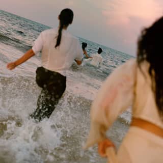 Guests run fully-clothed into the ocean froth at sunset, following a Temazcal ritual, seen from behind on the diagonal.