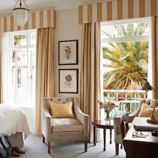 Light-filled hotel room with large bed and mustard yellow striped curtains