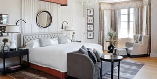 White walls offset chic monochrome soft furnishings in a Deluxe Suite bedroom with a large bed, bay window and chaise longue.