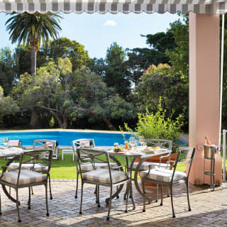 View from the Oasis Bistro terrace over tables with wine and lunch plates to the pool, surrounded by verdant lawn and trees.