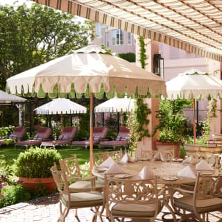 A laid table with eight chairs awaits guests on Oasis Bistro's terrace, where a canopy and parasols create abundant shade.