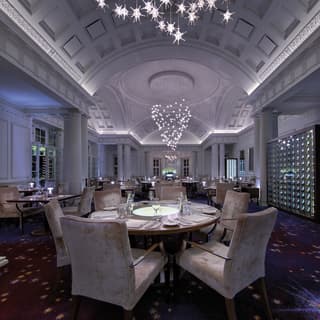 Laid tables with grey velour chairs anticipate a dining event in the atmospheric Planet Room with star-like cluster lights.