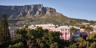 Aerial view of a pink hotel among lush foliage and Table Mountain beyond