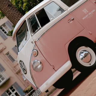 Angled image of a classic pink and cream Volkswagon camper van, branded with the Mount Nelson Hotel logo on the side.