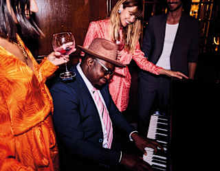 Man playing the piano surrounded by smiling guests at a party