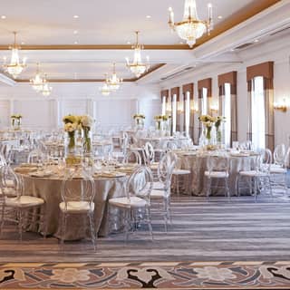 Wedding feast tables with camel cloth and white flowers fill the Ballroom, with its parquet floor and glittering chandeliers.