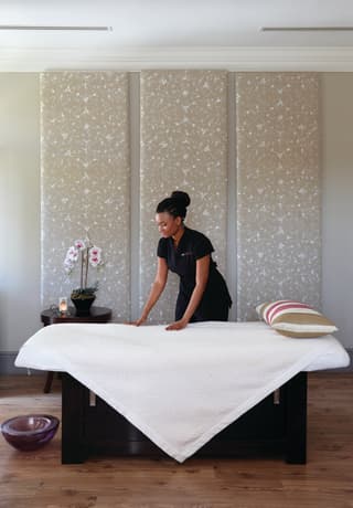 Spa therapist preparing a massage table in a light, contemporary treatment room>