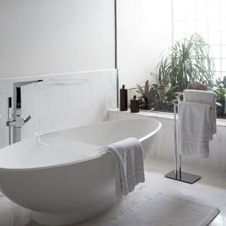 Modern standalone bathtub in a marble bathroom overlooking a balcony garden