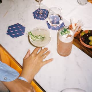 Looking down on a marble-top table with hexagonal blue coasters at Tragaluz, where guests enjoy cocktails with olives.