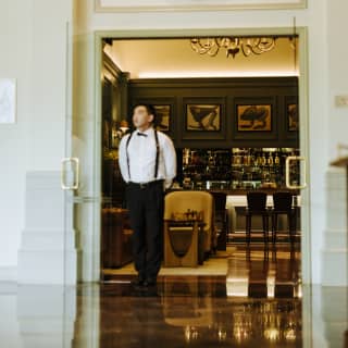 Exterior shot of Belo Bar's entrance as a staff member stands in the open doorway with views into the warm-lit interior.