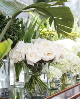 Polished wood side-table covered in vases filled with white roses and peonies
