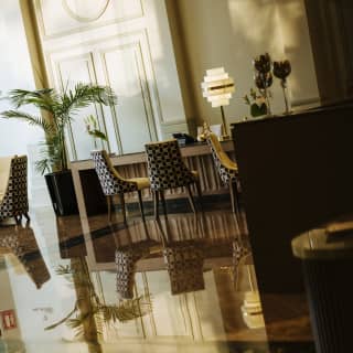 Angled image of three chairs at a desk with an opaline Art Deco table lamp, reflected in the highly polished lobby floor.